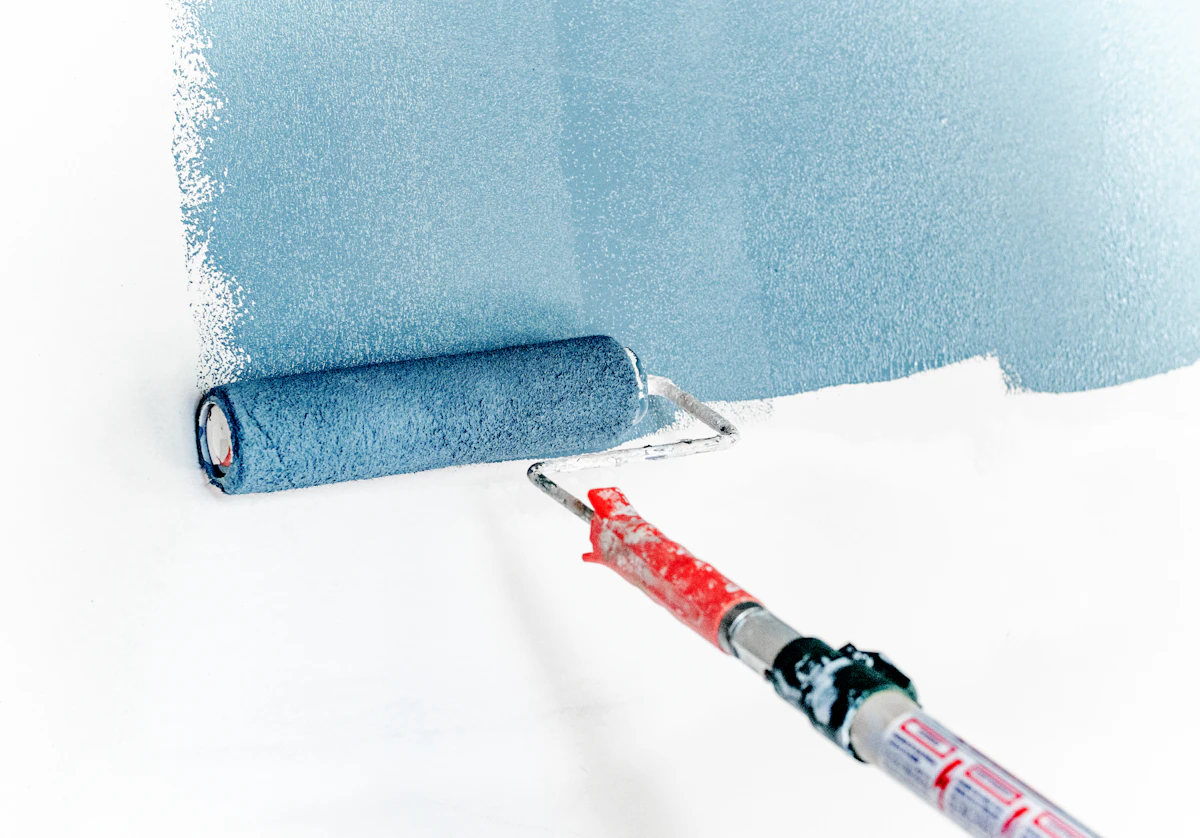 Rodillo extendiendo pintura azul sobre una pared blanca.